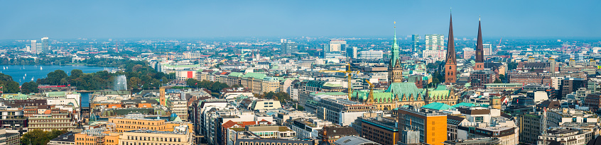 Aerial panorama over the spires and rooftops of central Hamburg, from the iconic tower of the Rathaus to the blue waters of Binnen Alster lake, Germany.