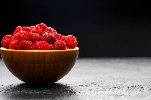 Photo of raspberries in wooden cup on black background