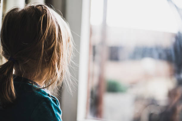 istock Back view of small girl looking through window. 1141190488
