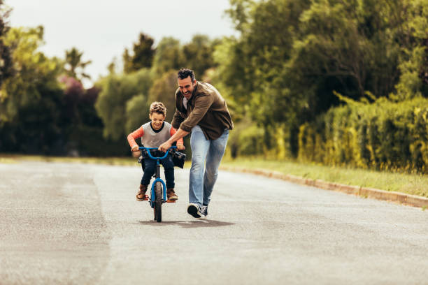 Father teaching his son to ride a bicycle Kid riding a bicycle while his father runs along holding the bicycle. Happy kid having fun learning to riding a bicycle with his father. son stock pictures, royalty-free photos & images