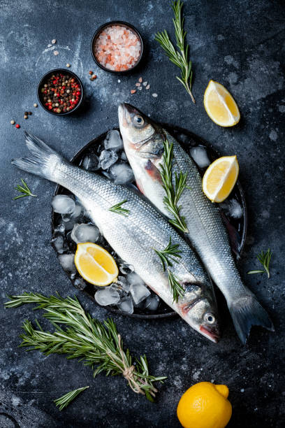 istock Fresh raw seabass fish on black stone background with spices, herbs, lemon. Culinary seafood background with ingredients for cooking. Top view 1141194249