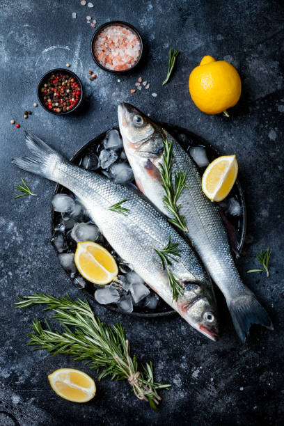 istock Fresh raw seabass fish on black stone background with spices, herbs, lemon. Culinary seafood background with ingredients for cooking. Top view 1141194352