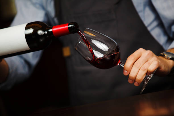 Man pouring wine into wineglass, male hand holding bottle Man pouring wine into wineglass, male hand holding bottle of red expensive alchoholic beverage, closeup photo sommelier photos stock pictures, royalty-free photos & images