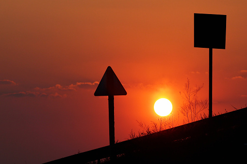 Silhouettes of traffic signs against the red sun at sunset