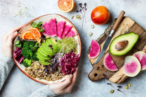 Photo of Girl holding vegan, detox Buddha bowl with quinoa, micro greens, avocado, blood orange, broccoli, watermelon radish, alfalfa seed sprouts.