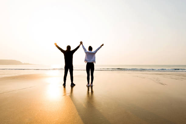 istock Couple standing at beach with arms raised 1141197630