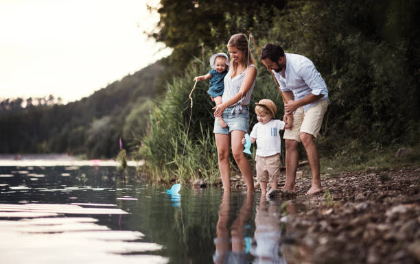 una giovane famiglia con due bambini piccoli all'aperto vicino al fiume in estate. - fun time foto e immagini stock