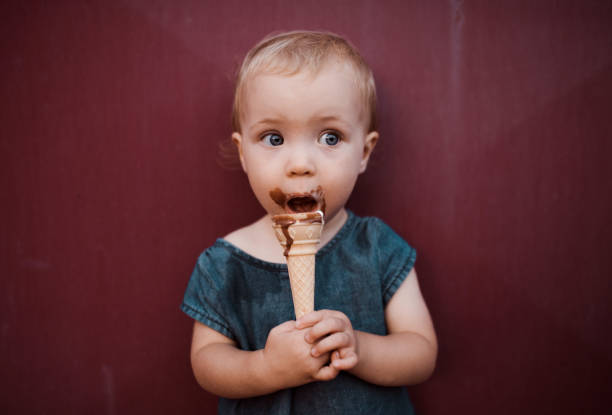 une vue de face de la petite fille de bambin à l’extérieur en été, mangeant la crème glacée. - ice cream people food recreational pursuit photos et images de collection