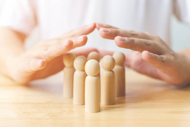 concept de protection des personnes de santé et d’assurance. bouclier de main protègent l’homme en bois sur la table - sauvegarde photos et images de collection