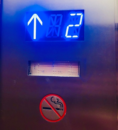 Brightly lit number 2 in neon blue color in the metal elevator and with a no smoking sign
