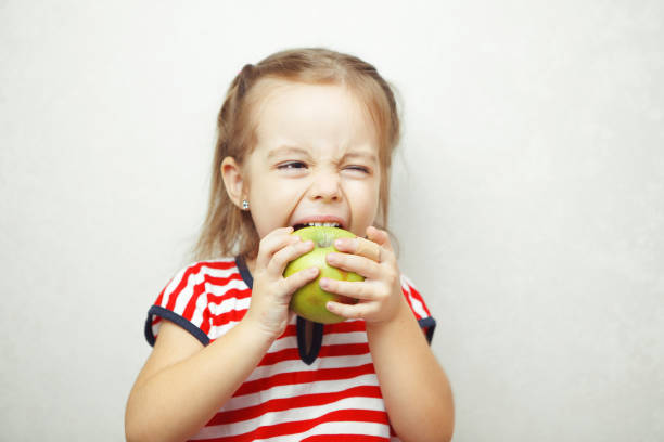 istock Kid with cute hairstyle holding and eating green apple 1141205352