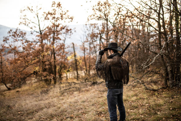 Rear view with cowboy holding hat and rifle on his shoulder, outdoor