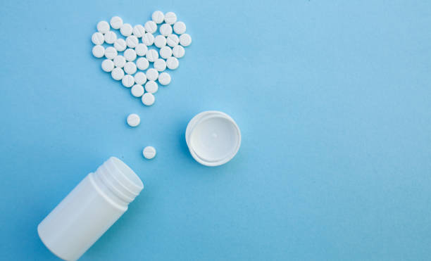 medicine, healthcare and pharmacy concept - pills and of drugs in shape of the heart medicine, healthcare and pharmacy concept - pills and of drugs in shape of the heart white tablets are laid out in the shape of a heart and white plastic jar on a blue background with copy space aspirin photos stock pictures, royalty-free photos & images