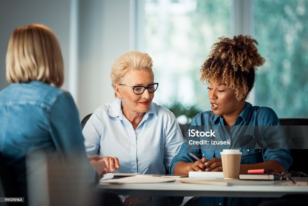 Businesswoman talking with executives at desk Businesswoman talking with executives at desk. Business professionals are working on start-up. They are sitting in office. Mature Women Stock Photo