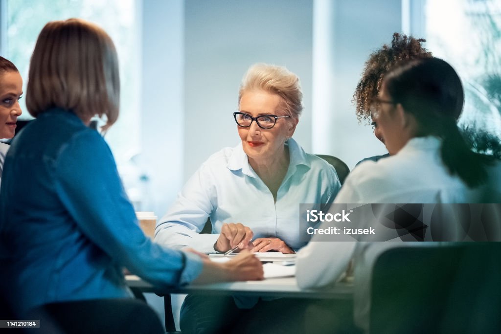 Businesswomen having meeting at desk in office Businesswomen having meeting at desk in office. Senior expertise is advising new plans to colleagues. Female professionals are working on start-up business. Businesswoman Stock Photo