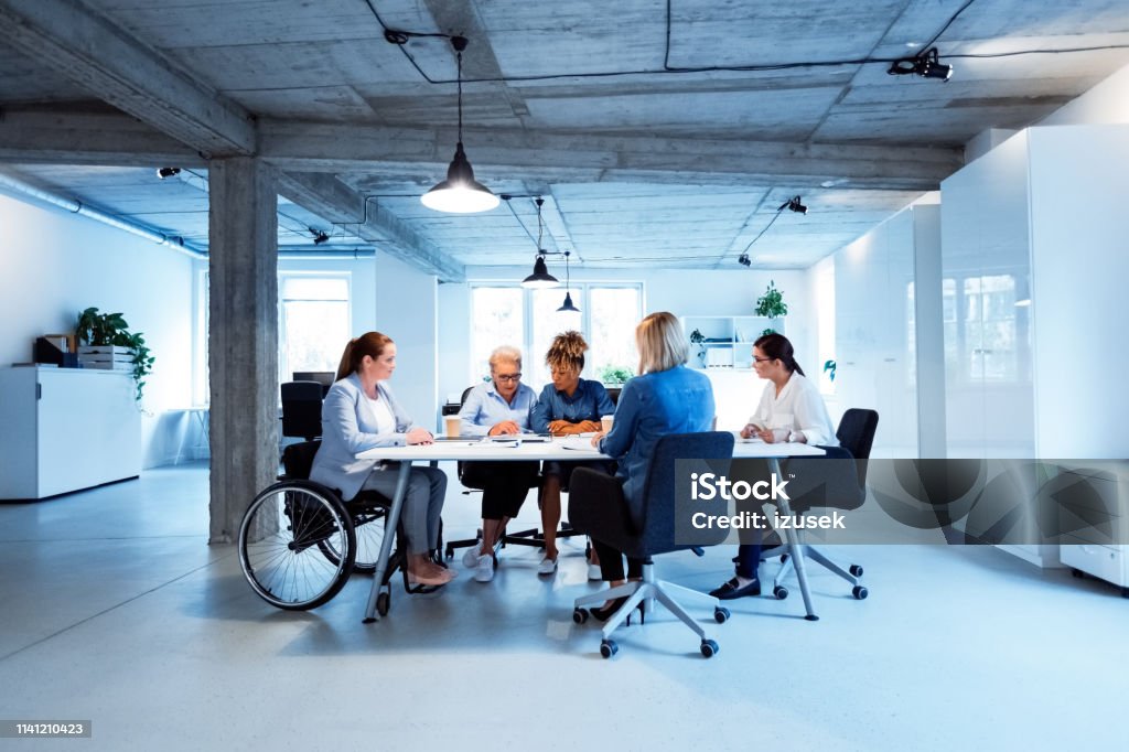 Female entrepreneurs having meeting in new office Female entrepreneurs having meeting in new office. Executives are planning new business strategies. They are working at desk. Wheelchair Stock Photo