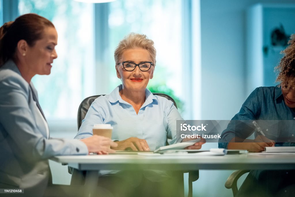 Portrait of confident smiling senior businesswoman Portrait of confident smiling senior businesswoman. She is sitting with colleagues in new office. They are working on start-up business. 35-39 Years Stock Photo