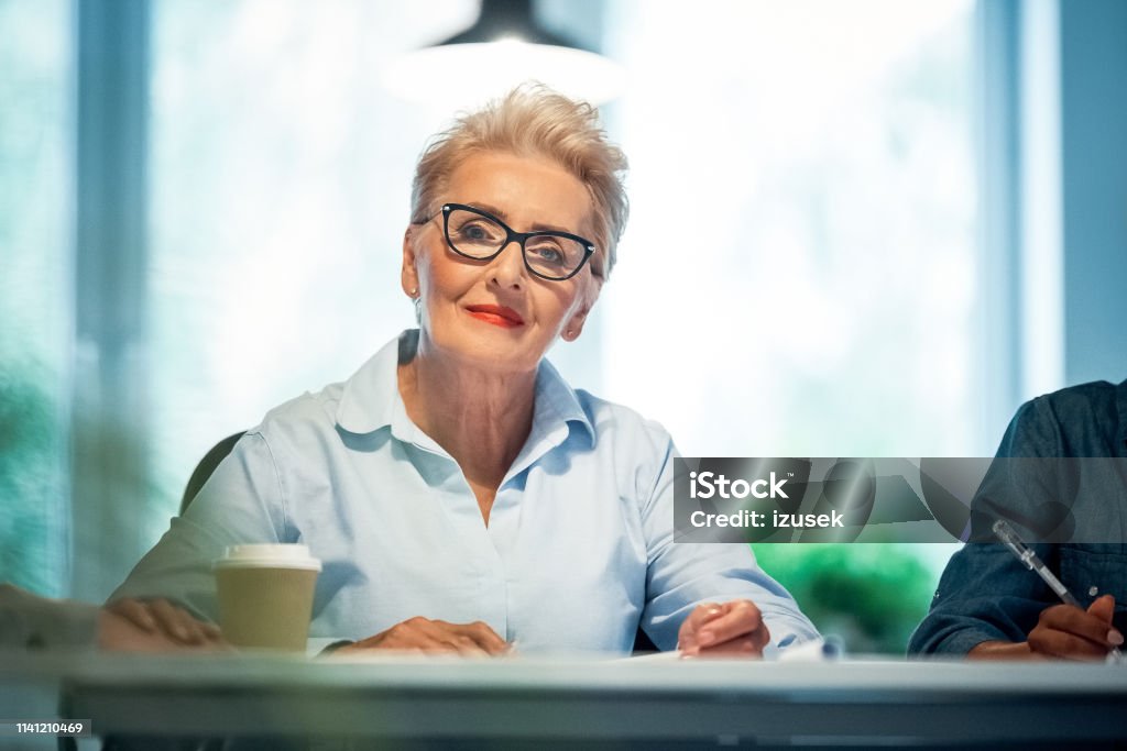 Portrait of senior professional working in office Portrait of confident senior businesswoman working in office. Female expertise is wearing eyeglasses and shirt. She is working on start-up business. Owner Stock Photo