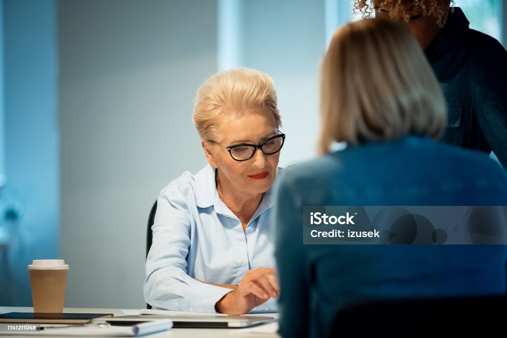 Senior woman working with colleagues in new office Senior businesswoman working with colleagues in office. Female expertise are concentrating on their new business. Elderly professional is wearing eyeglasses. 35-39 Years Stock Photo