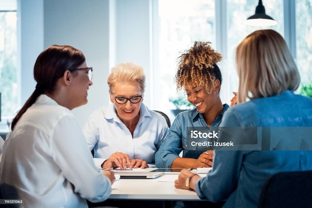 Smiling businesswomen working in new office Smiling businesswomen working at desk in new office. Confident female executives are planning strategies. Senior expertise is advising colleagues. 35-39 Years Stock Photo