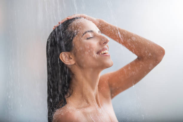 Positive woman taking hot shower Side view beaming lady locating under stream of water. She holding hair with arms woman hot shower stock pictures, royalty-free photos & images
