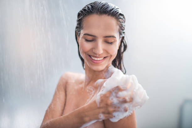 Smiling female rubbing body with foam Portrait of happy girl taking shower with gel. She washing with puff foam material photos stock pictures, royalty-free photos & images