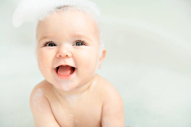 ein baby mädchen badet in einem bad mit schaum und seifenblasen - baby or kind stock-fotos und bilder