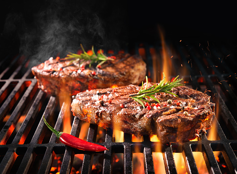 Beef steaks sizzling on the grill with flames