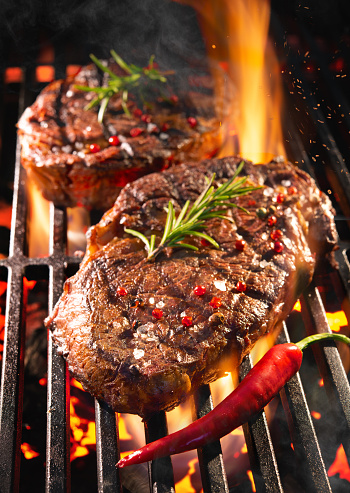 Beef steaks sizzling on the grill with flames