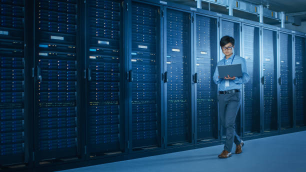 istock In the Modern Data Center: IT Engineer Working with Server Racks, Uses Laptop for Maintenance and Diagnostics. Checking Stability of the System 1141224874