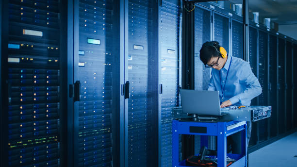 istock In the Modern Data Center: IT Technician Wearing Protective Headphones Working with Server Racks, on a Pushcart Installing New Hardware. Engineer Doing Maintenance and Diagnostics of the Database. 1141224916
