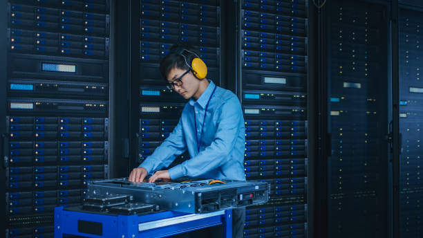 istock In the Modern Data Center: IT Technician Wearing Protective Headphones Working with Server Racks, on a Pushcart Installing New Hardware. Engineer Doing Maintenance and Diagnostics of the Database. 1141224932