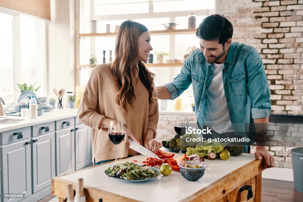 Doing everything together. Beautiful young couple cooking dinner and drinking wine while standing in the kitchen at home Adult Stock Photo