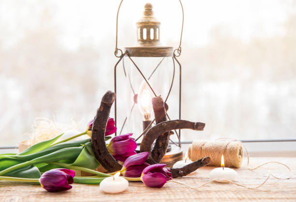 istock Old rusty horseshoes, brown vintage lantern with modern dimmable decorative light bulb switched on and white candles lit and  tulips on wooden window sill. Horseshoe Vastu Shastra good luck symbol. 1141230597