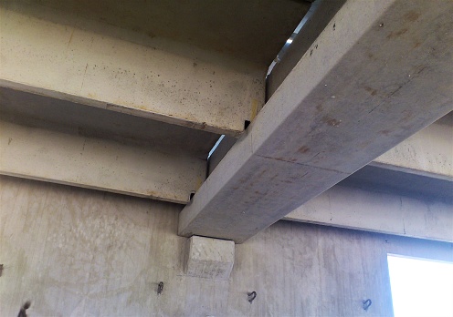 A precast concrete parking garage under construction with an i girder and double tee beams sitting on its ledges.