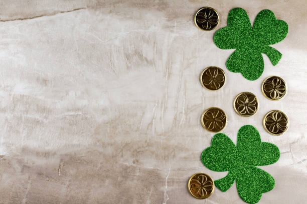istock Two green glittery shamrocks with gold coins on tan stone tile background. 1141234312