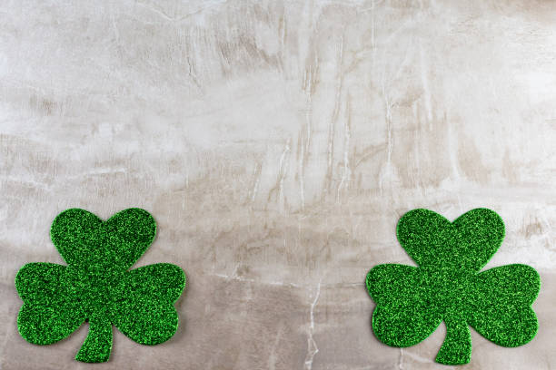 istock Two green glittery shamrocks, one in each bottom corner, on a tan stone tile. 1141234603