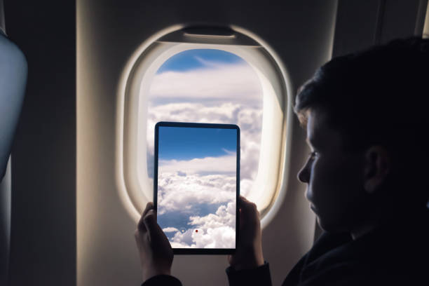 istock Caucasian boy using tablet pc taking picture through airplane window clouds with sky. 1141237874