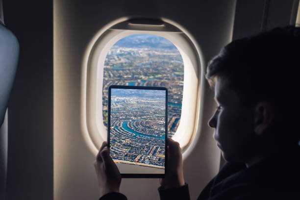istock Caucasian boy using tablet pc taking picture through airplane window Redwood Shores State Marine Park and Foster city. San Francisco. California. USA 1141237909