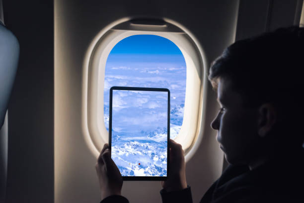 Caucasian boy using tablet pc taking picture through airplane window Greenland glaciers.