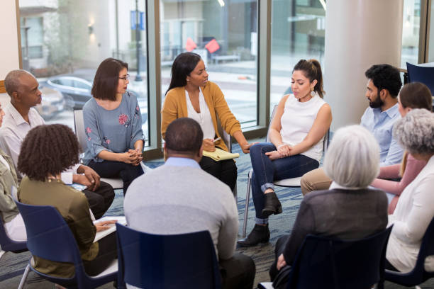 Mental health professional comforts woman Upset mid adult woman discusses a difficult issue during a support group meeting. A caring mental health professional comforts and speaks encouraging words to the woman. group therapy photos stock pictures, royalty-free photos & images