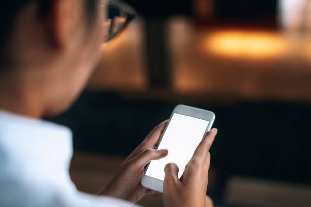 istock Woman wearing glasses using a smartphone read and text messages with blank space screen display from behind view- woman office worker- digital and communication concept 1141239963