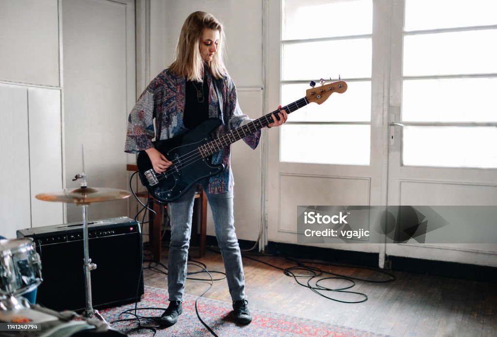 Female Bass Guitarist On Rehearsal Generation Z Music Band On Rehearsal. Selective focus on girl with bass guitar. Bass Guitar Stock Photo
