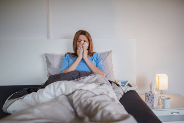 istock Woman lying sick in bed with a flu, blowing her nose 1141246742