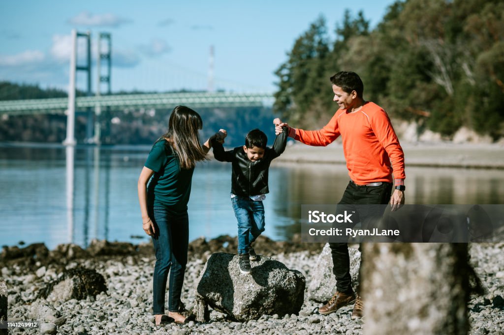 Playful Loving Indian Family At Beach Together A young family spends time together at a Puget Sound beach in Washington state, enjoying the time outdoors with each other.  The father and mother carry their little boy in their arms. Family Stock Photo