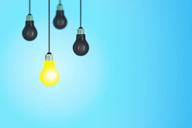 istock Business Idea Concept : One yellow light bulb of others black light bulb hanging from ceiling with blue background. 1141250687
