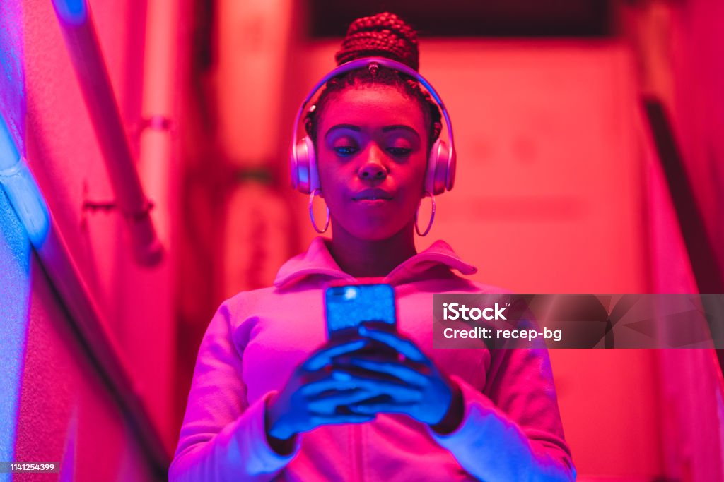 Portrait of young black woman listening to music under neon lights A portrait of a young black woman while she is listening to music under neon lights. Technology Stock Photo