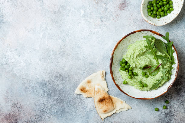 Green pea hummus spread or dip with mix salad leaves. Healthy raw summer appetizer, vegan, vegetarian snack. Copy space stock photo