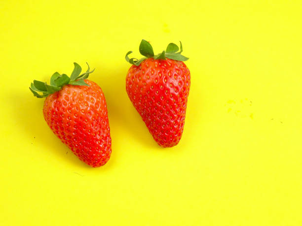 istock Two Isolated Strawberries, lighted with a warm light  on a bright yellow background 1141277007