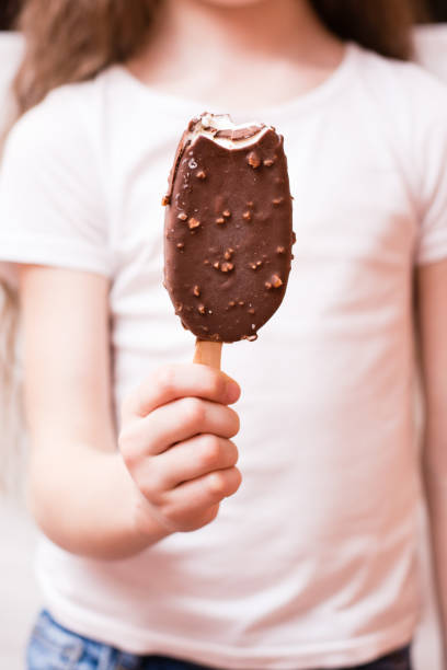 istock The girl holds in her hand a bitten popsicle in chocolate icing with nuts 1141284186